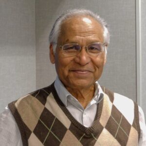 A gray-haired man wearing a diamond plaid sweater vest.